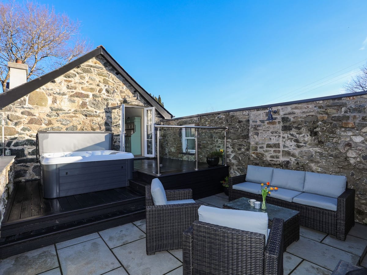 Walled stone courtyard at Bryn Moelyn Cottage with hot tub on decking and wicker sofa seating