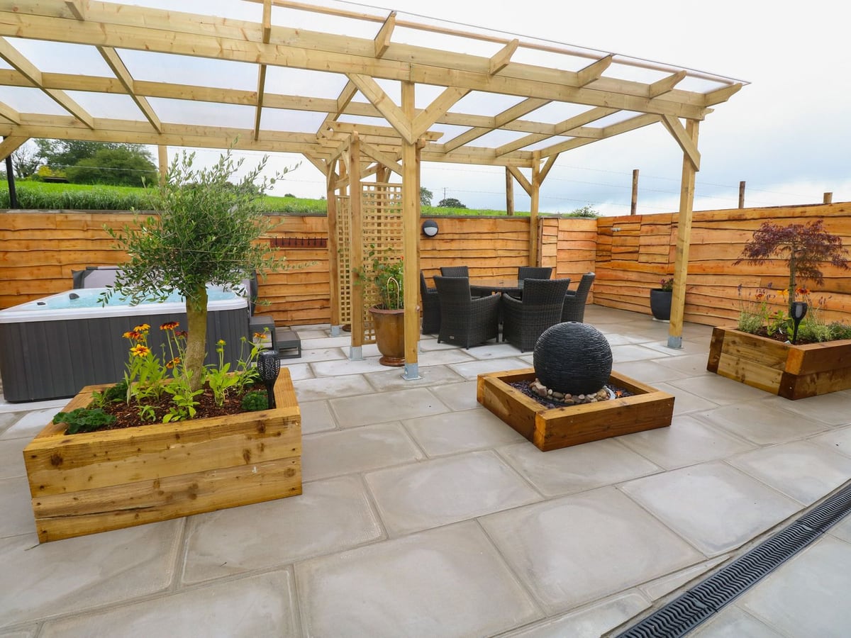 Brynawel paved patio with pergola, rattan dining set, raised planters and hot tub by timber fencing