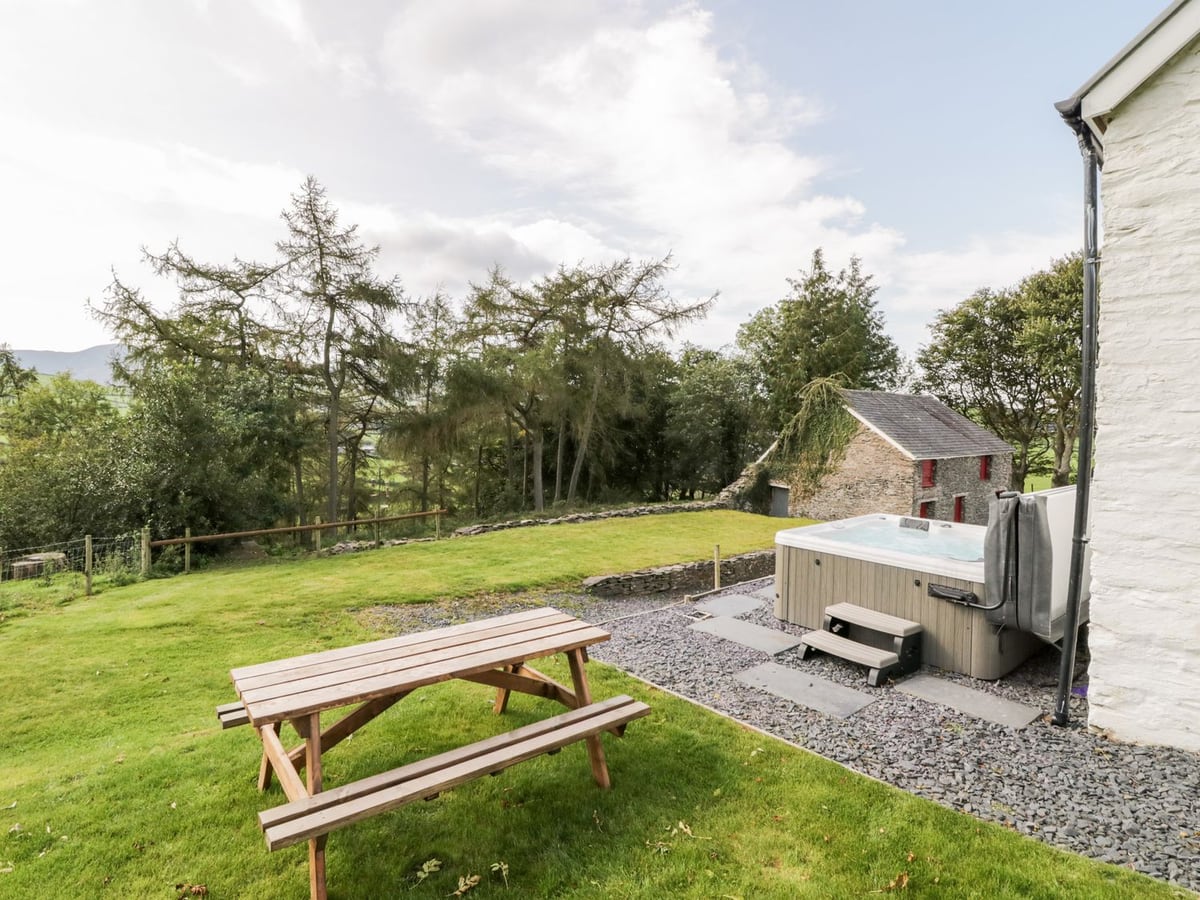 Lawn with a picnic bench beside Bryndan, with a hot tub on slate gravel and a stone outbuilding