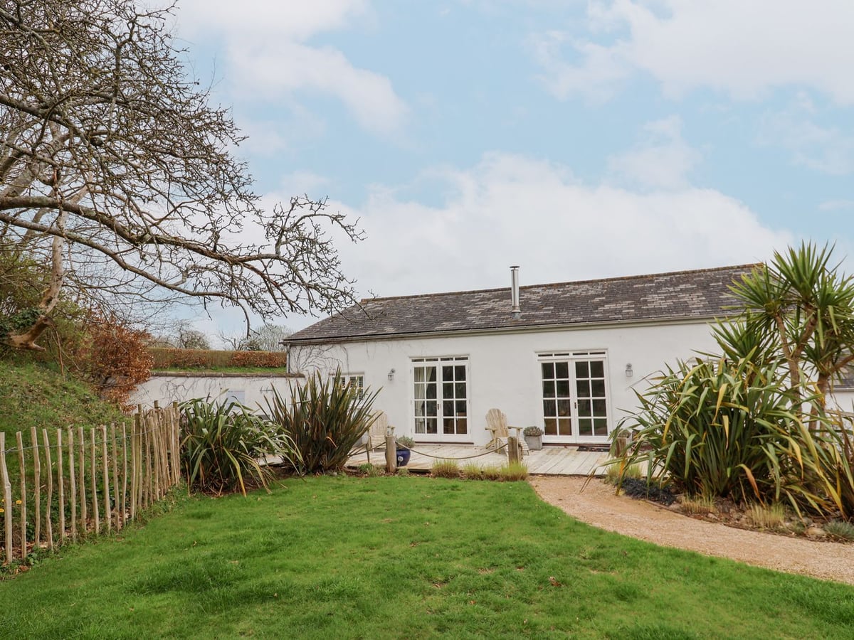 White cottage with glazed garden doors, decking and a planted lawn outside Burrows