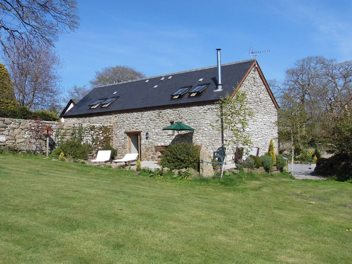 Stone walls and glazed doors facing the lawn and outdoor seating at Butterdon Barn