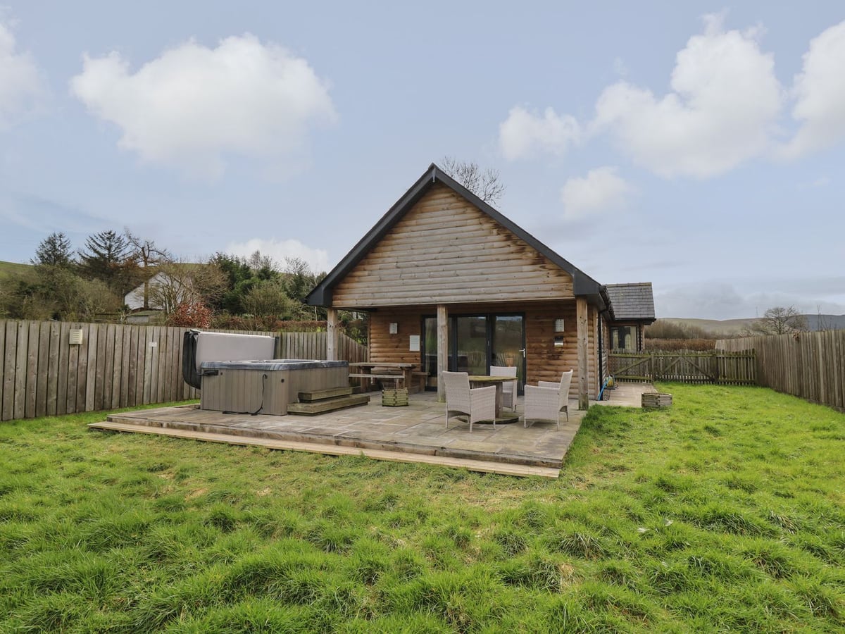 Caban Dulas timber lodge with a hot tub, patio seating and a lawn bordered by timber fencing