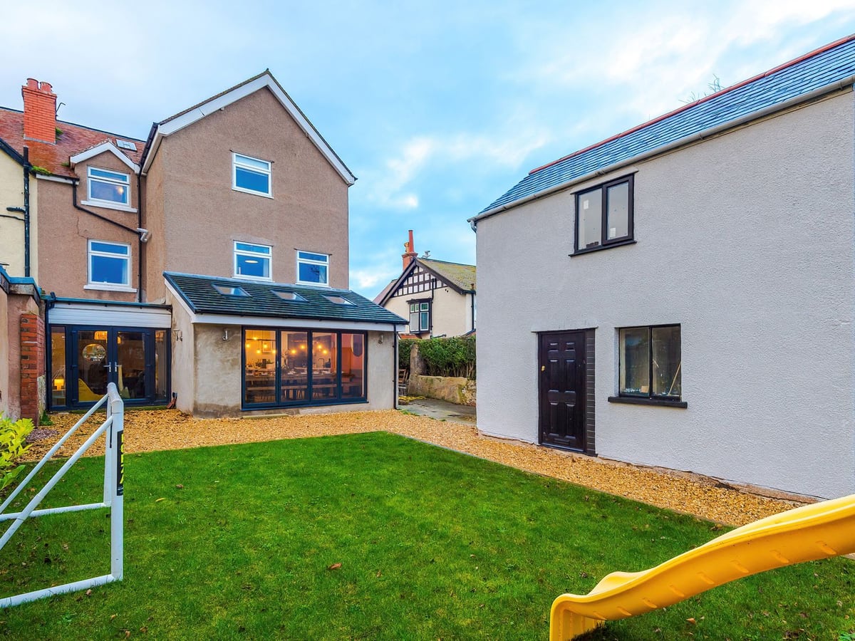 Rear lawn and gravel garden at Cabin Hill, with a glazed dining extension, outbuilding and play slide