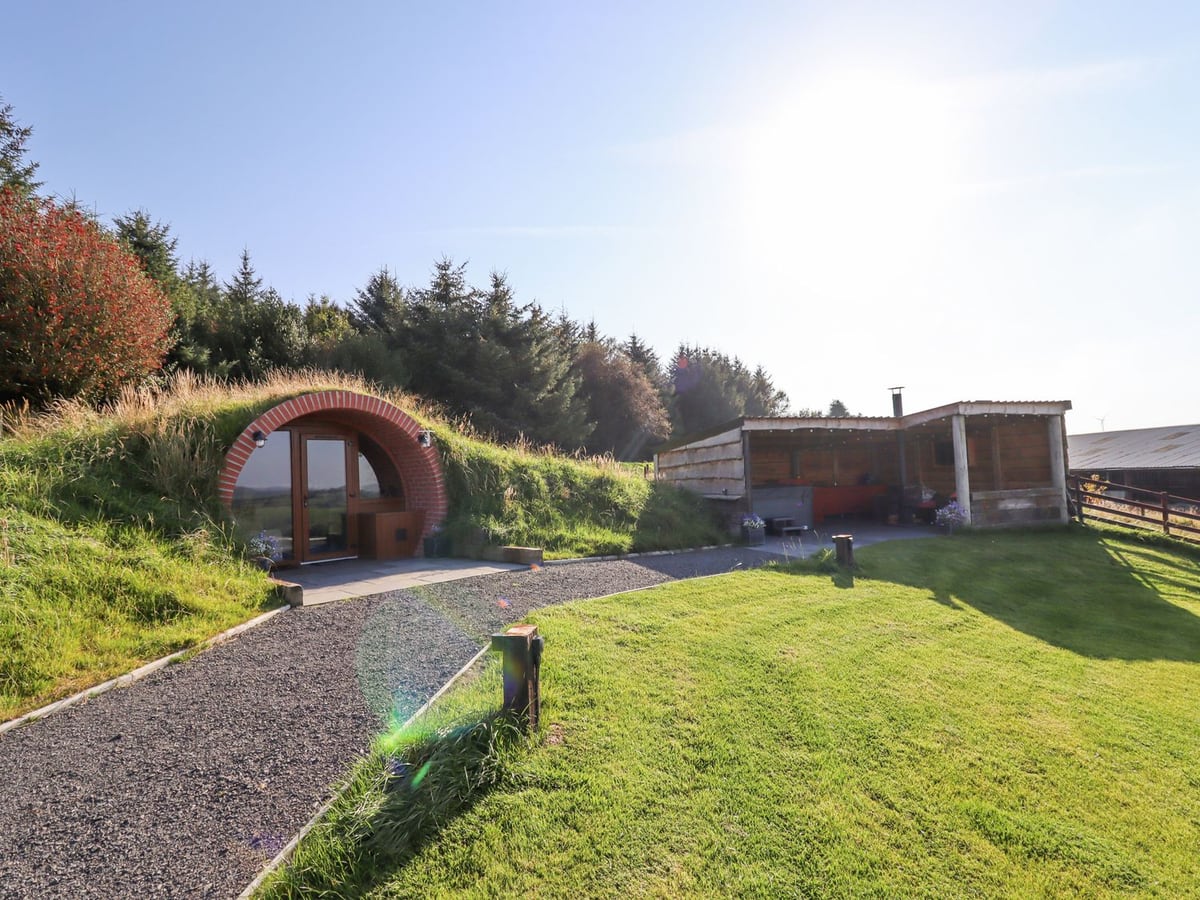 Cae Bach grass-covered pod with a round brick doorway, gravel path, lawn and open-sided timber shelter