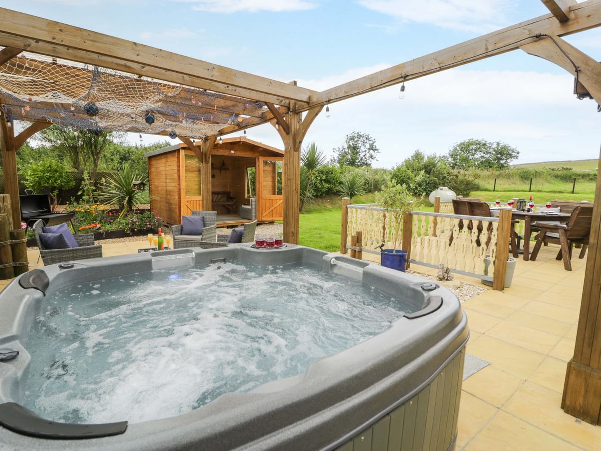 Cae Berllan hot tub under a pergola beside a patio, summerhouse and lawn with fields beyond