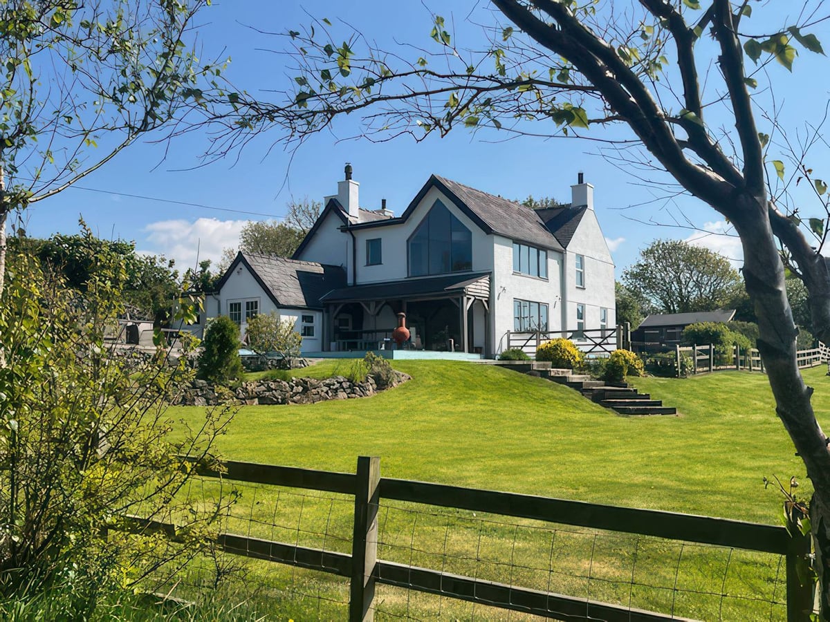 Cae Du house and sloping lawn with garden steps, trees and a fence across the foreground