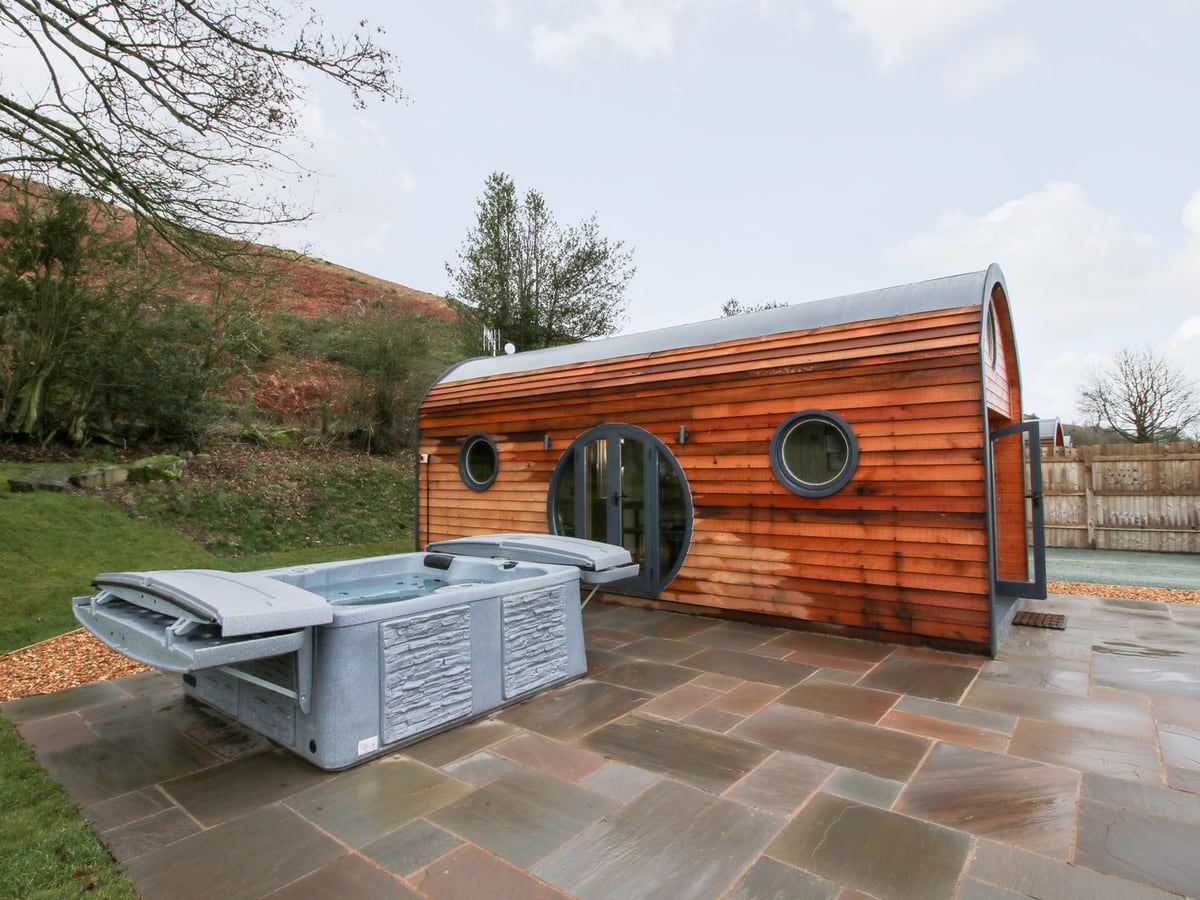 Callow Pod's timber side with round windows, a paved terrace and square hot tub