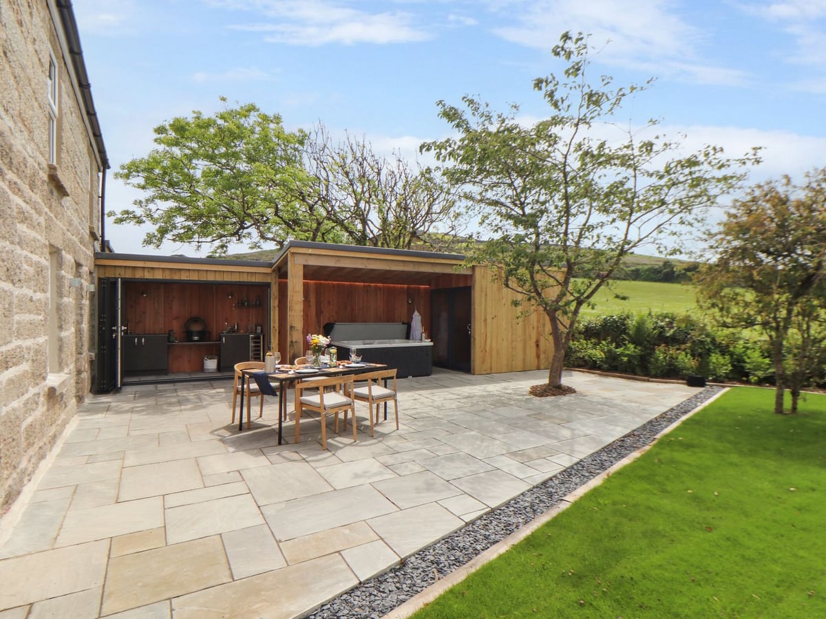 Carn House patio and lawn beside a timber shelter containing a hot tub and outdoor kitchen