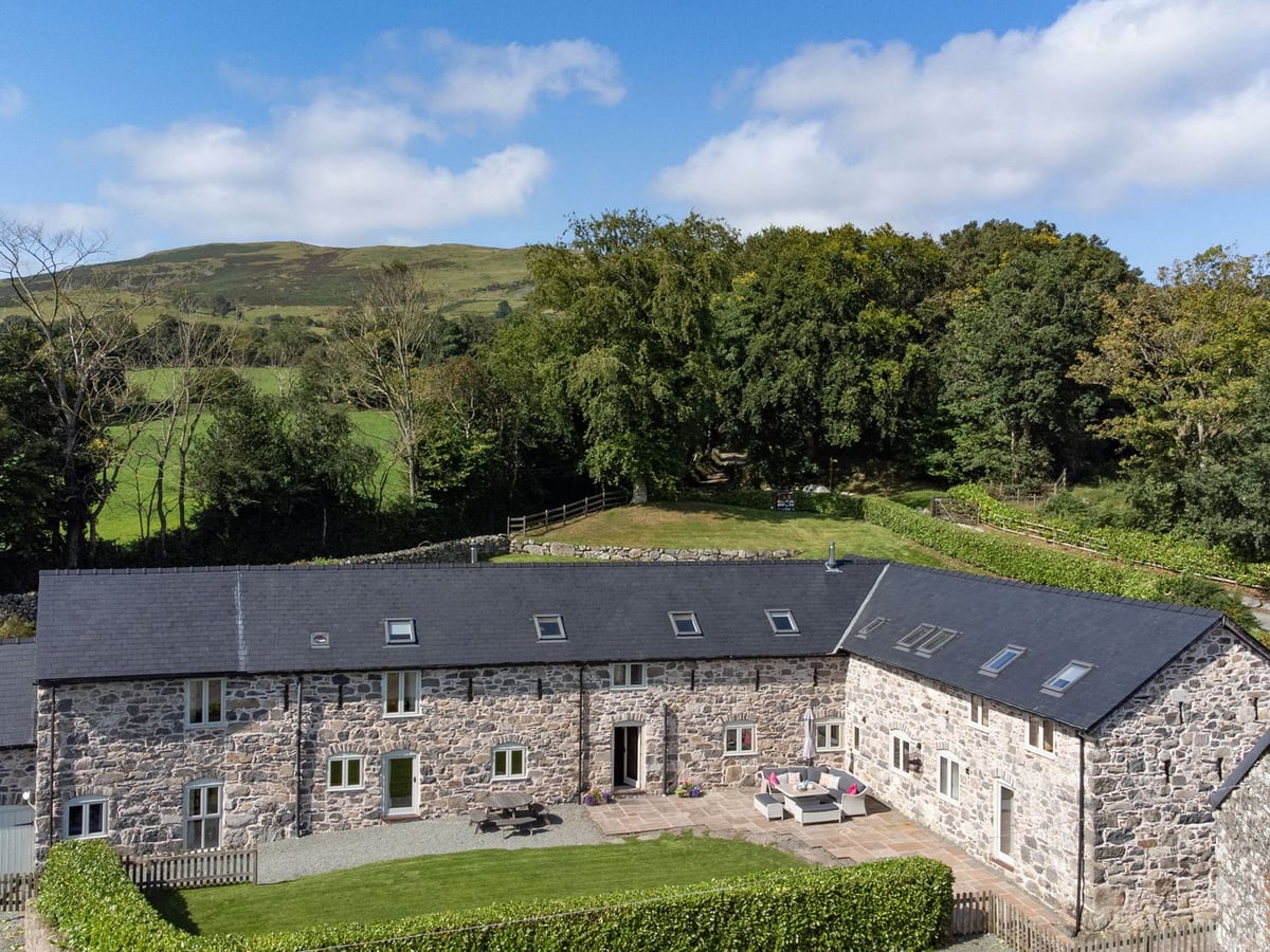 Aerial view of Castell Courtyard stone barn with hedged front lawn, patio seating and wooded hills
