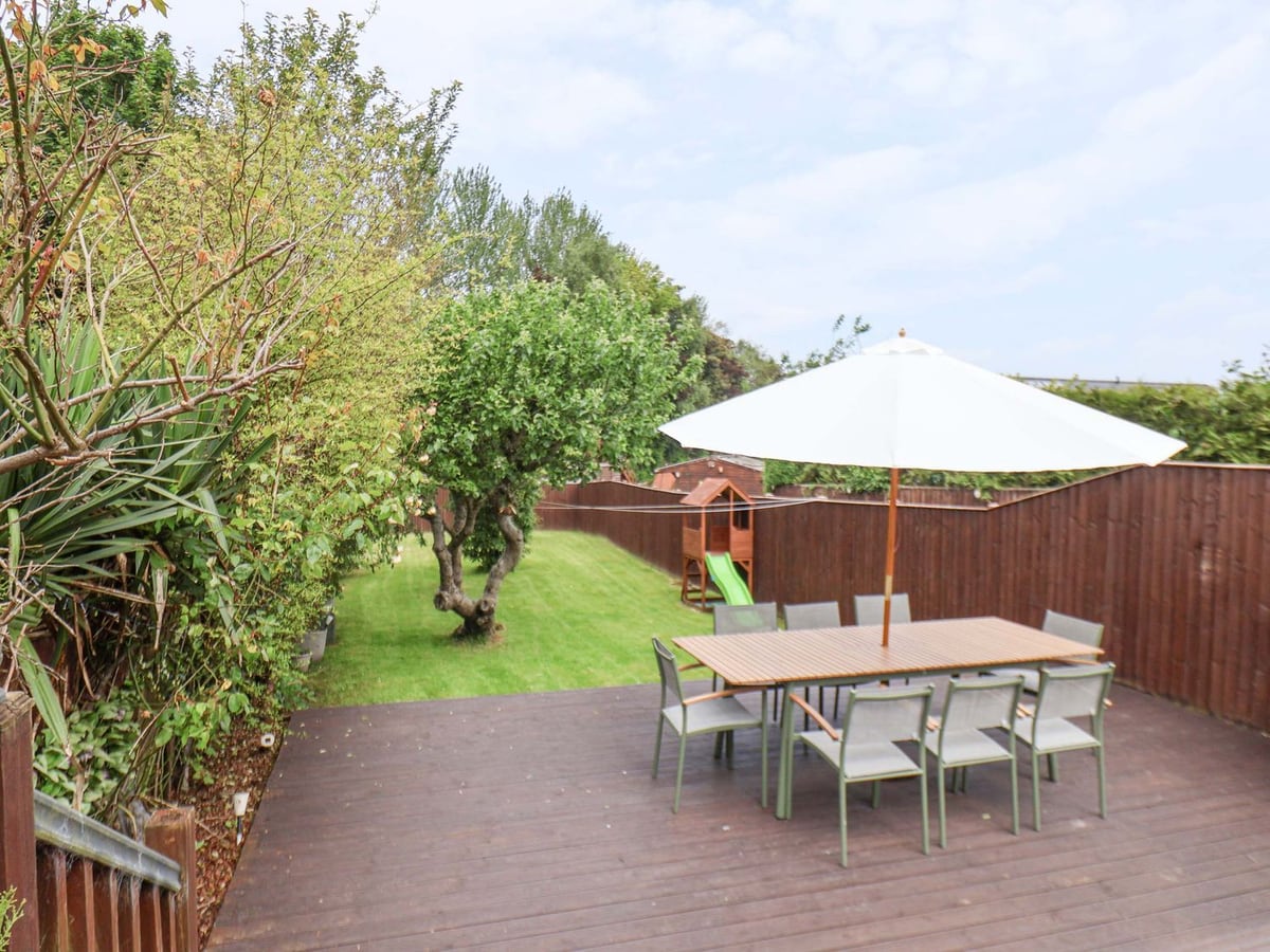 Lawn and trees beyond a deck with a dining table, parasol and chairs at Castle View