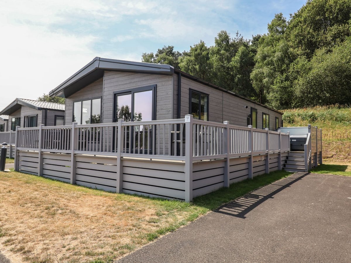 Grey lodge with raised decking, steps and a hot tub at Cedar Lodge three bedrooms