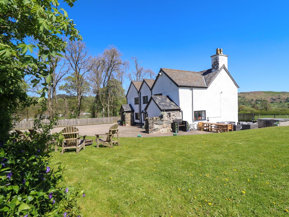 Cefn Nannau white farmhouse with a large lawn, wooden garden chairs, patio seating and a hot tub