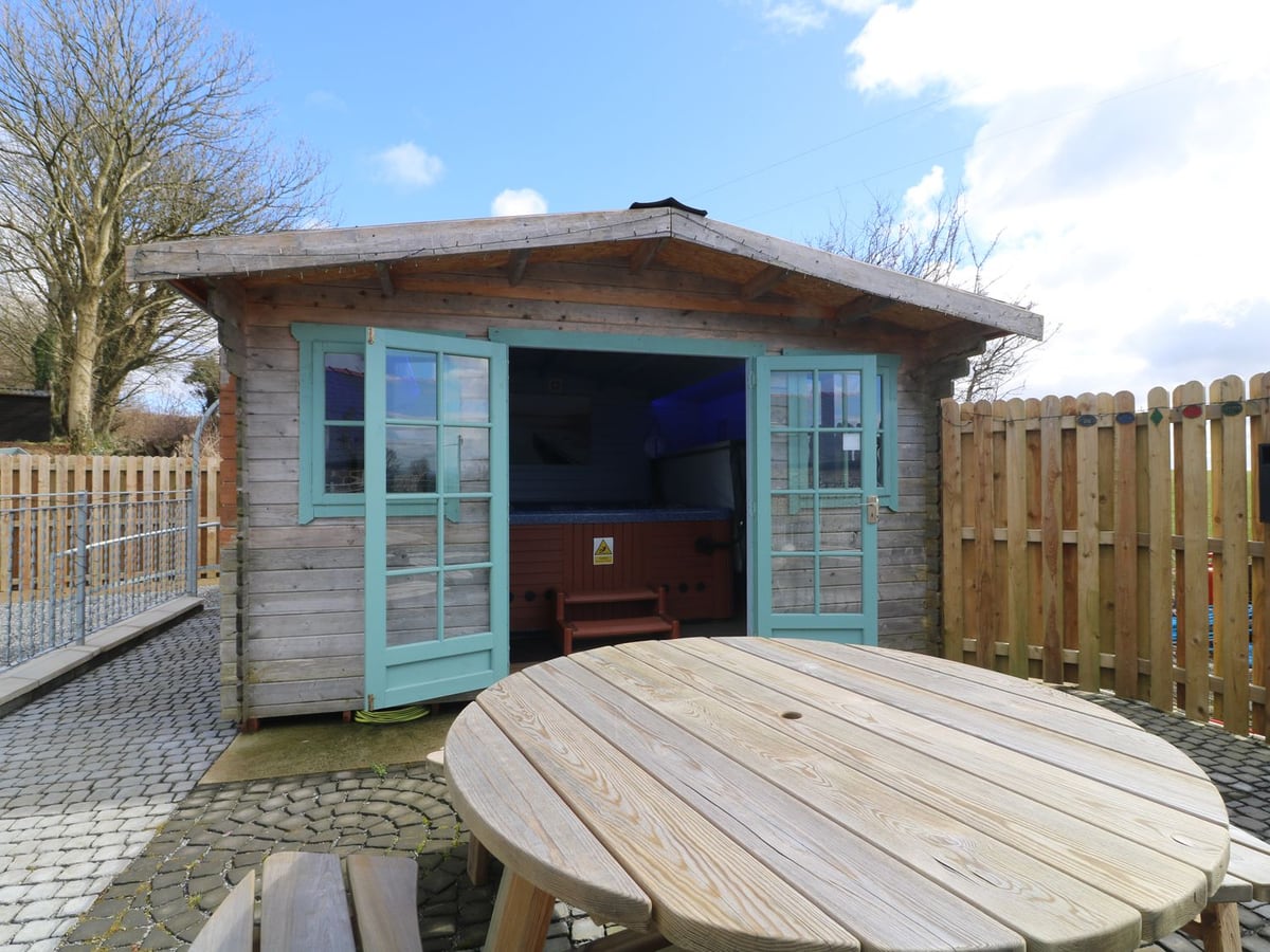 Hot tub cabin with open doors on a paved terrace at Cherry Cottage, with a picnic table and fencing