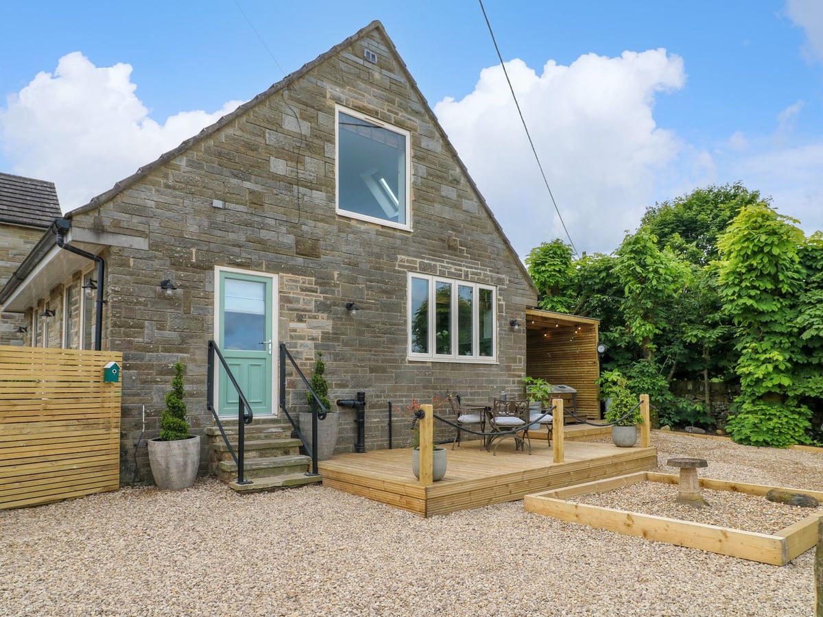 Cherry Tree Cottage stone exterior with a timber seating deck, gravel yard and hot-tub shelter