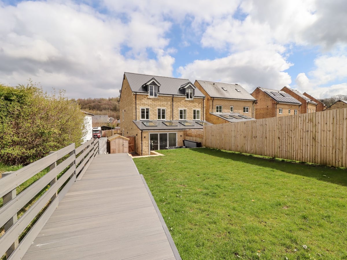 Lawn and grey decking leading to the stone house and rear patio at Cheshire View