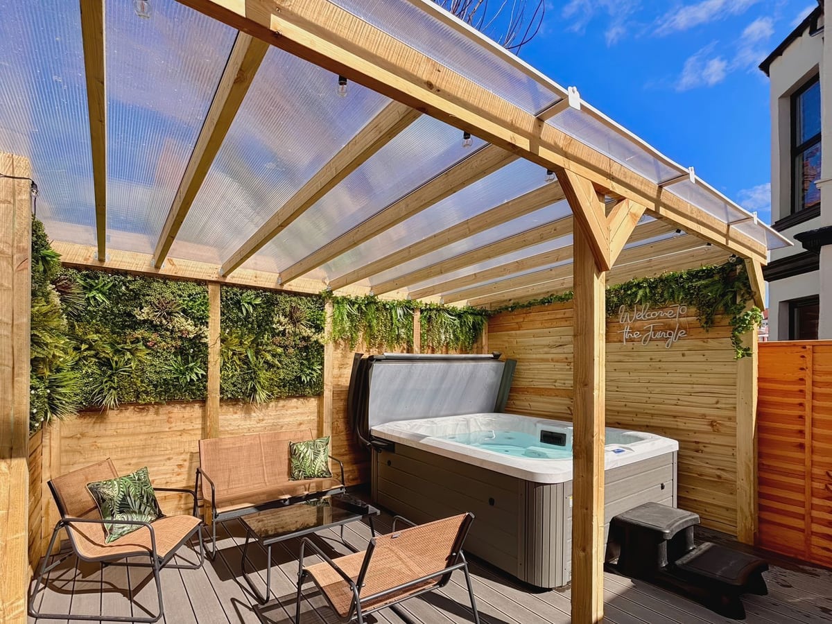 Decked courtyard at Clarence House with seating and an open hot tub under a clear pergola roof