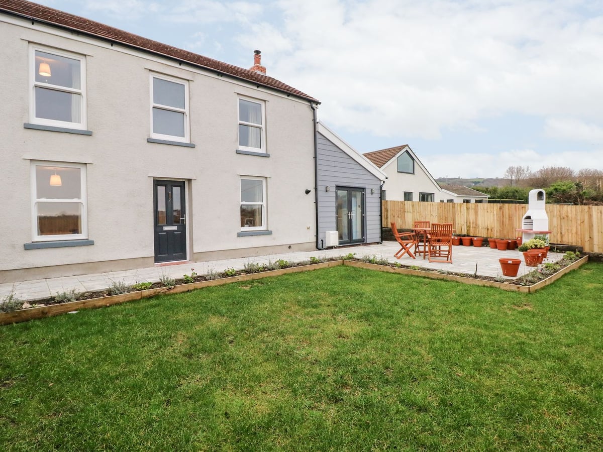 Coeden Bach white house with a lawn, planted borders and a fenced patio with table and chairs