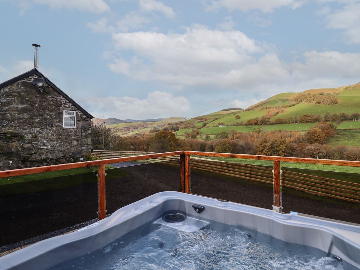 Collfryn hot tub on a fenced terrace with stone cottage and rolling hills beyond