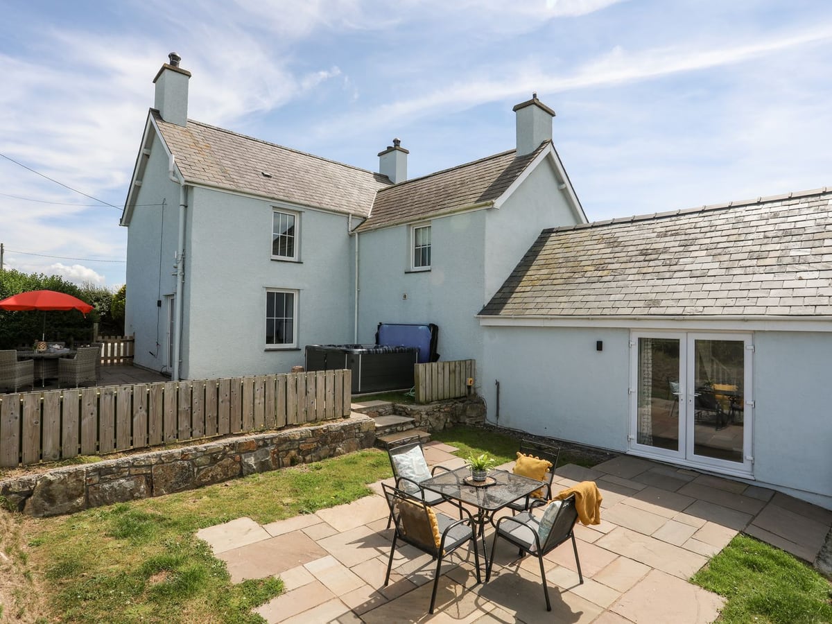 Congl Cae white house with a paved patio table, lawn, wooden fencing and a hot tub beside the house