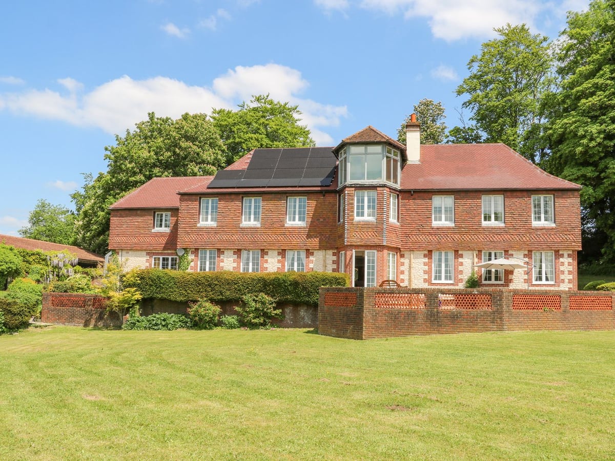 Coombe Place House brick exterior with lawn, red-tiled roof and trees behind