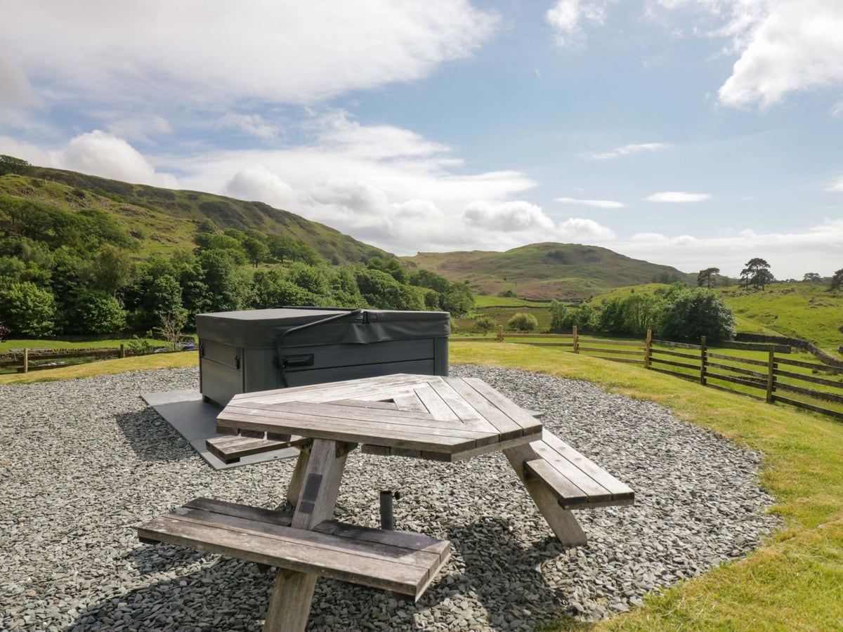 Picnic table and covered hot tub on gravel beside grass and field views at Copper Beech Cottage