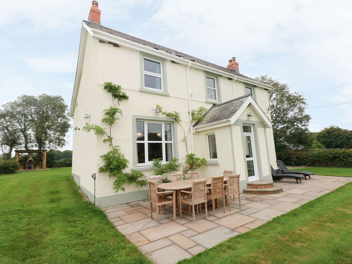 Copybush Cottage cream house with patio dining table, sun loungers and lawn on both sides