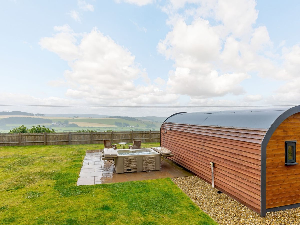 Corndon Pod beside a hot tub and fenced lawn, with fields visible beyond the garden