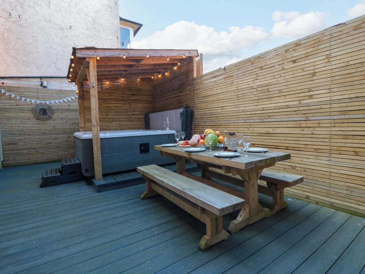 Decked rear courtyard with a picnic table and hot tub beneath a timber canopy at Coronation House