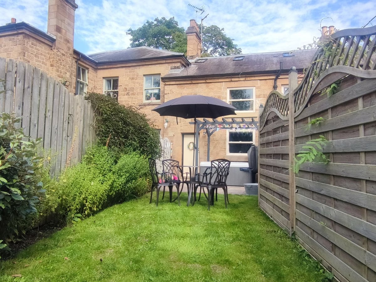 Narrow lawn and outdoor table between wooden fences behind the stone Courthouse Cottage
