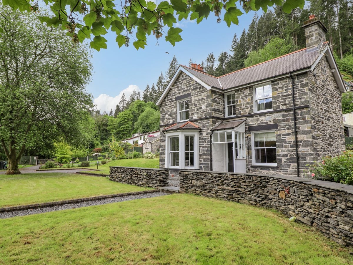 Craigside stone house behind a low slate wall, with open lawn in front and wooded hillside behind