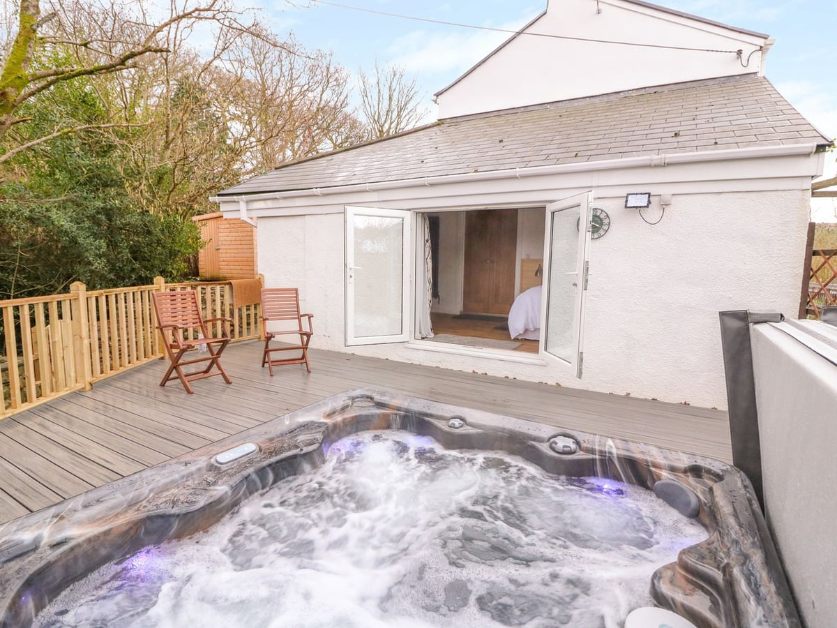 Crooked Hill Cottage deck with a bubbling hot tub, two folding chairs and open doors into a bedroom