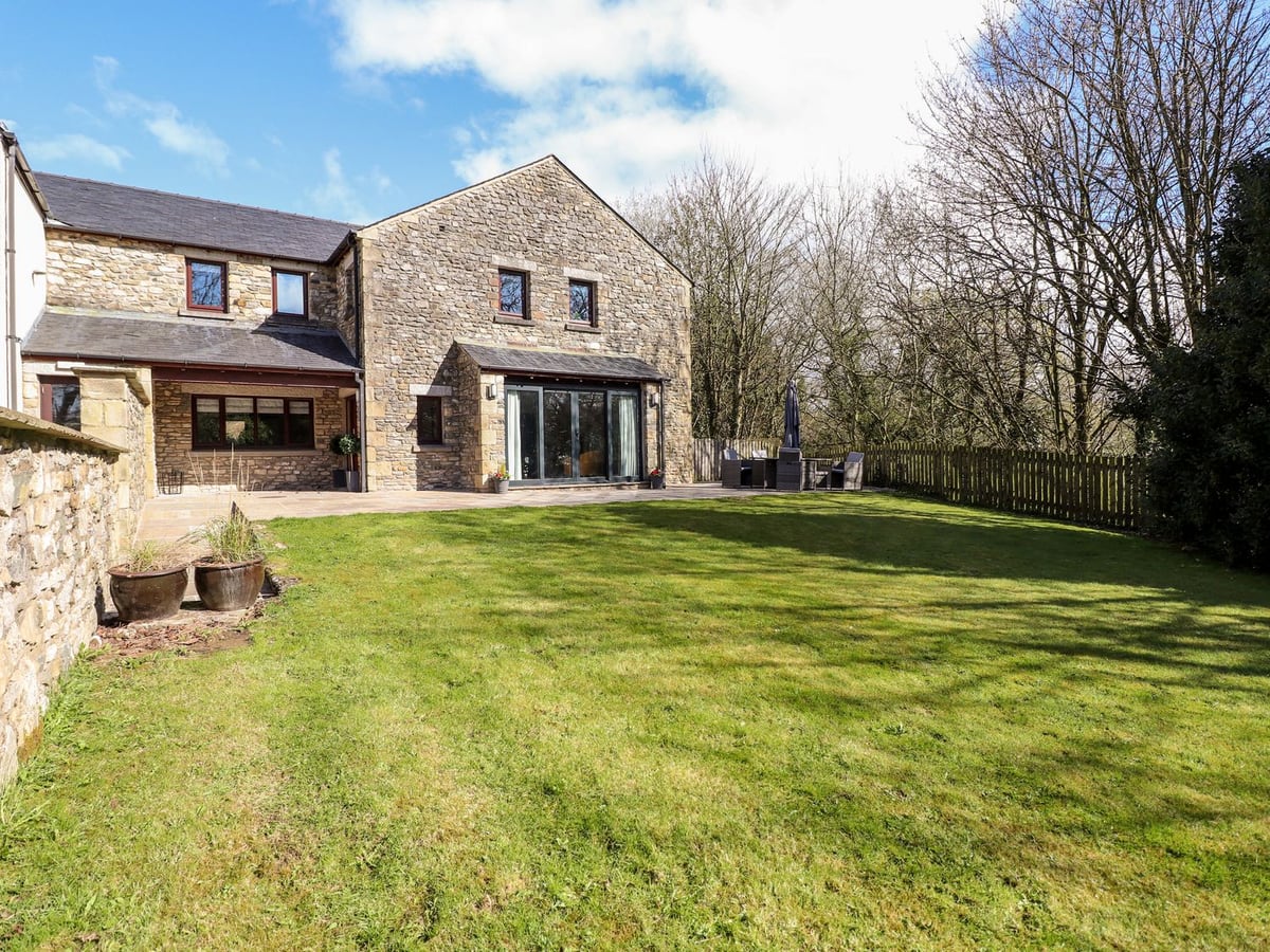 Crooklands Cottage stone exterior beyond a lawn, paved terrace and wooden boundary fence