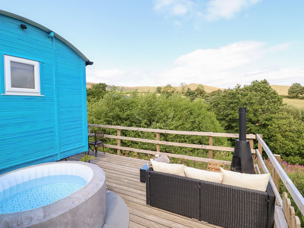 Cuckoo shepherd's hut deck with an inflatable hot tub, rattan sofa and chiminea overlooking wooded hills
