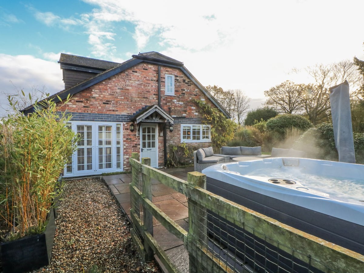 Hot tub on the fenced patio beside the red-brick exterior of Curlew Cottage