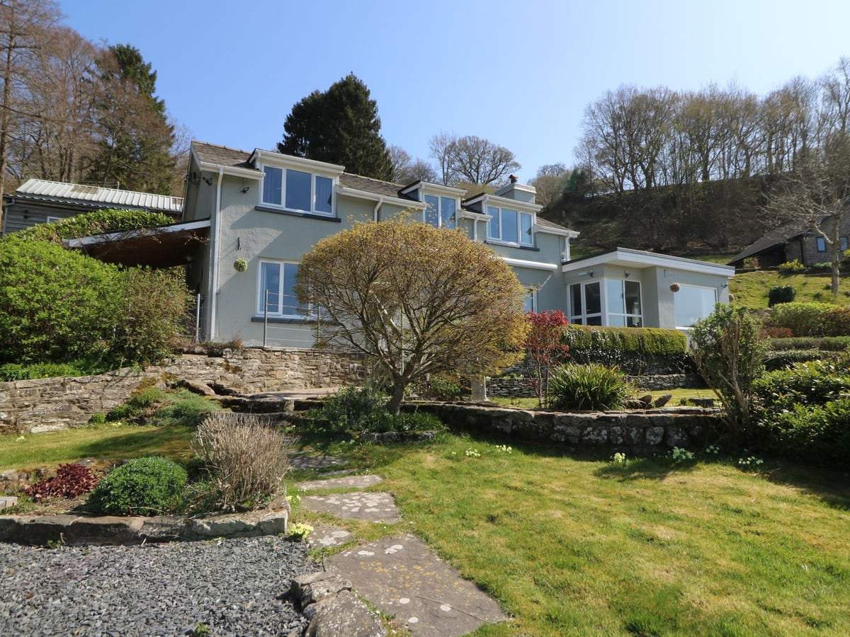 Grey rendered house above terraced lawns, stone walls, shrubs and a stepping-stone path at Curtau