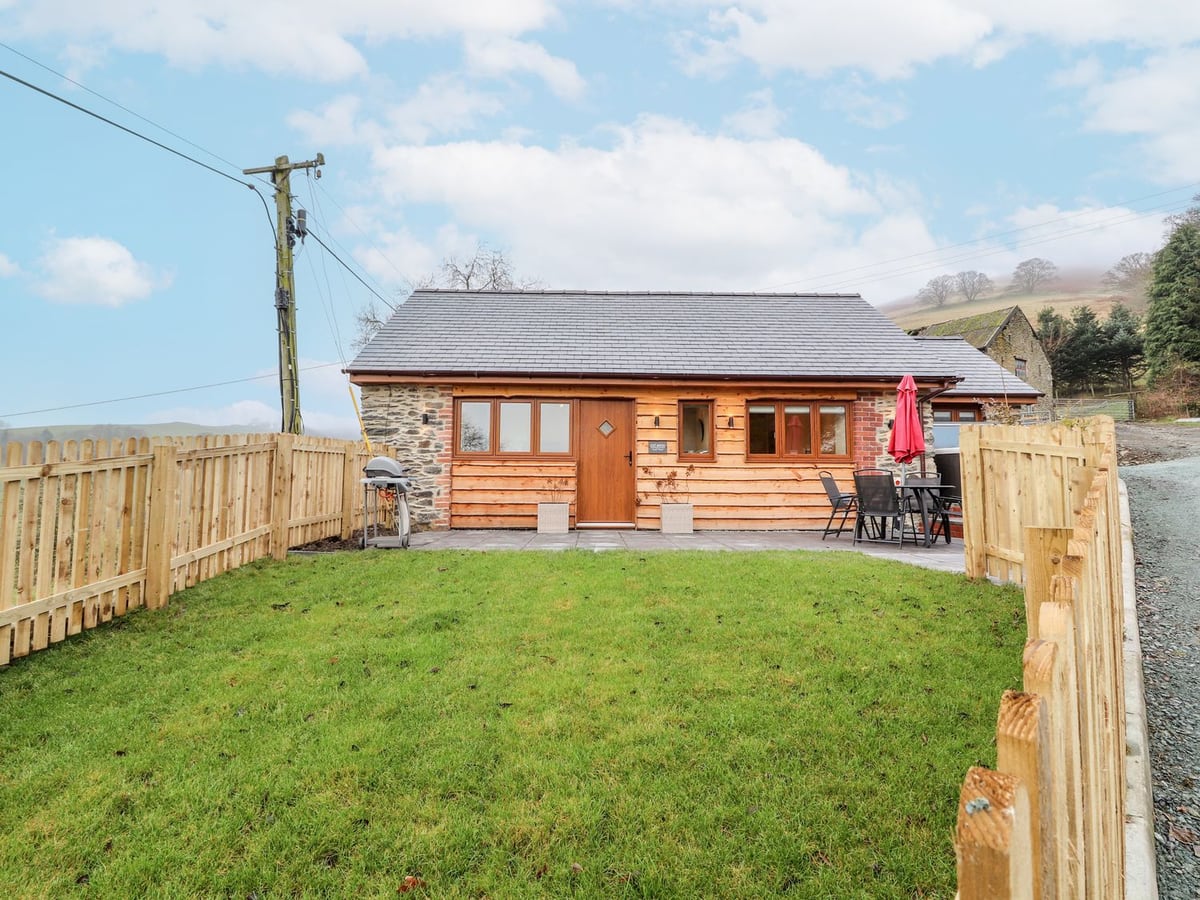 Cut Moch stone and timber cottage with fenced lawn, patio table, red parasol and barbecue