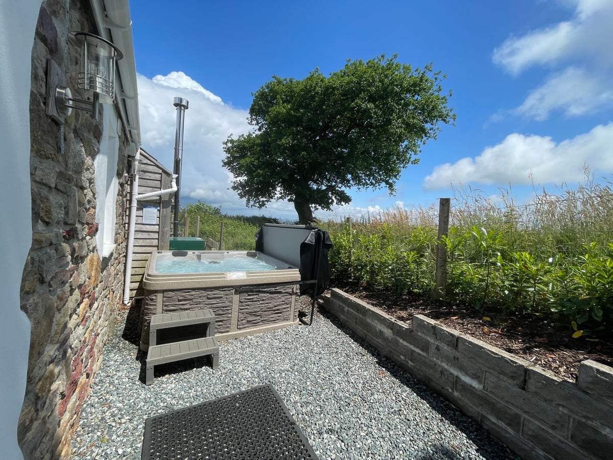 Hot tub with its lid raised on a gravel patio beside Dairy Cottage, next to a raised planting bed