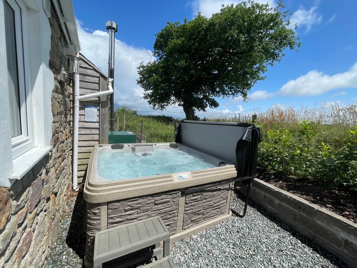 Hot tub on a gravel patio beside the stone wall of Dairy Cottage, with a tree beyond