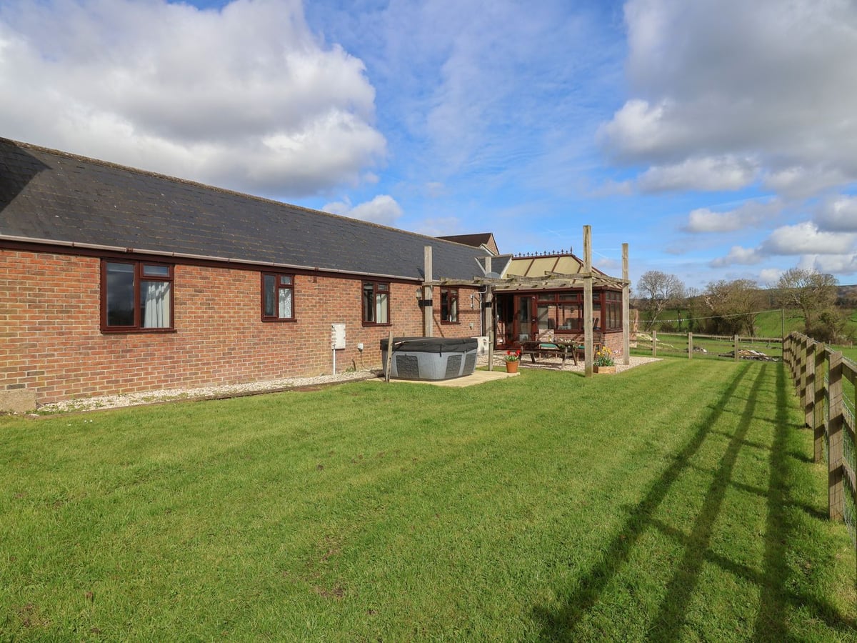 Daisy Cottage beside a long lawn, post-and-rail fence, conservatory and covered hot tub
