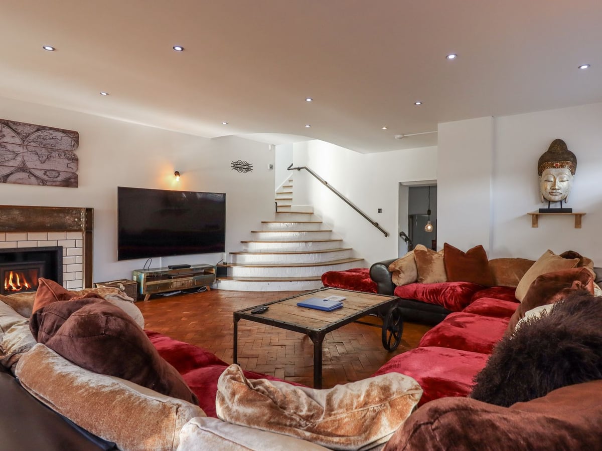 Lounge with red-covered sofas, fireplace and broad wooden staircase at Delmonte Lodge