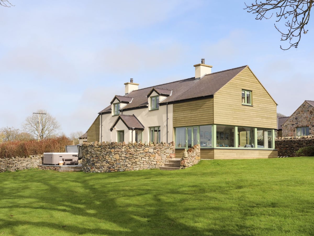 Dolwaenydd house with a large lawn, curved dry stone wall and a hot tub on a side patio