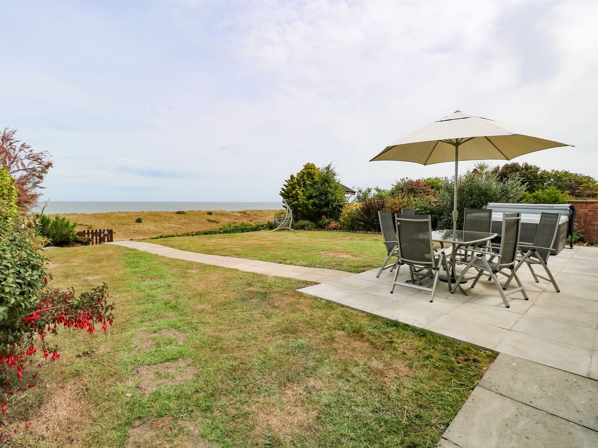 Lawn and patio seating beside the hot tub at Drifters, with dunes and sea beyond