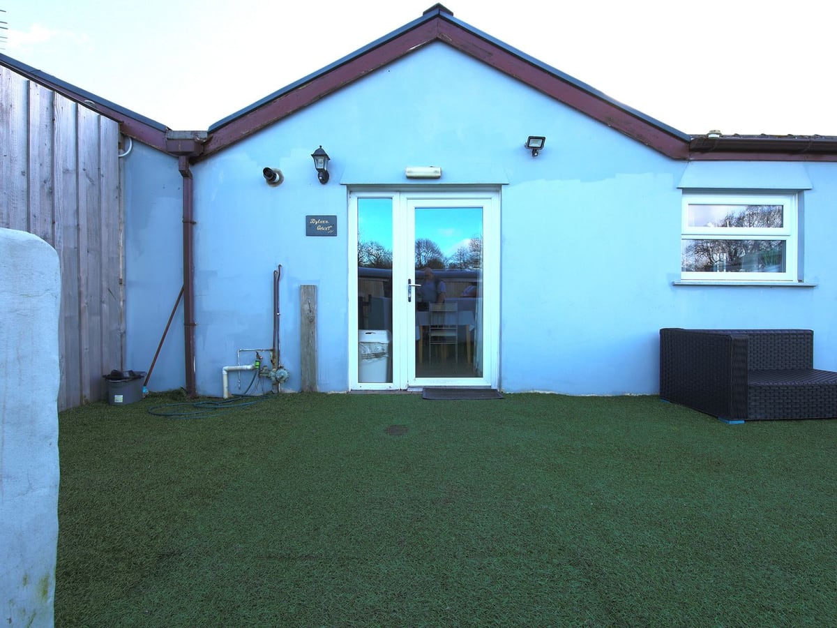 Blue-painted Dylan's Court with a glazed door facing artificial turf and a rattan-style corner seat