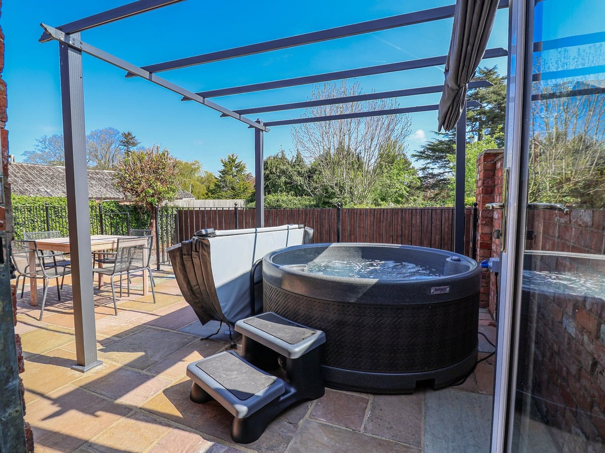 Elwy Cottage hot tub on a paved patio beneath a pergola frame, with a table, chairs and fencing