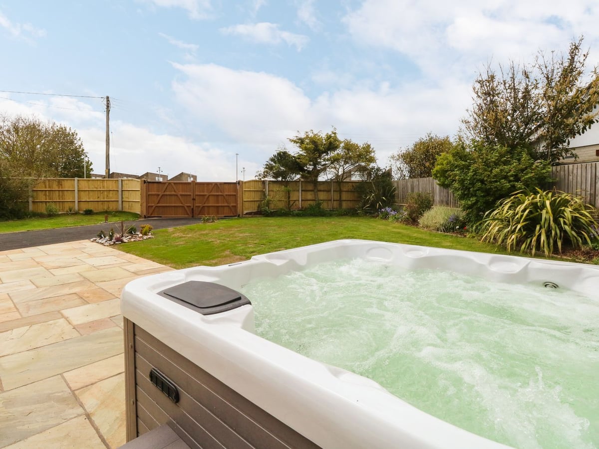 Hot tub on a paved patio beside lawn and timber gates at Fallowfield in Winterton-on-Sea