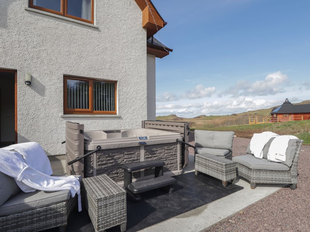 Hot tub and garden chairs beside Falls Cottage, with a timber barbecue hut and hillside beyond