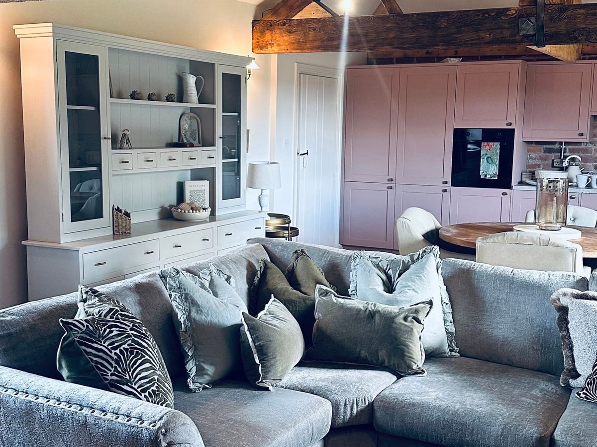 Grey sofa, cushions, pale dresser and exposed timber beams in the Farnah House Barn living room
