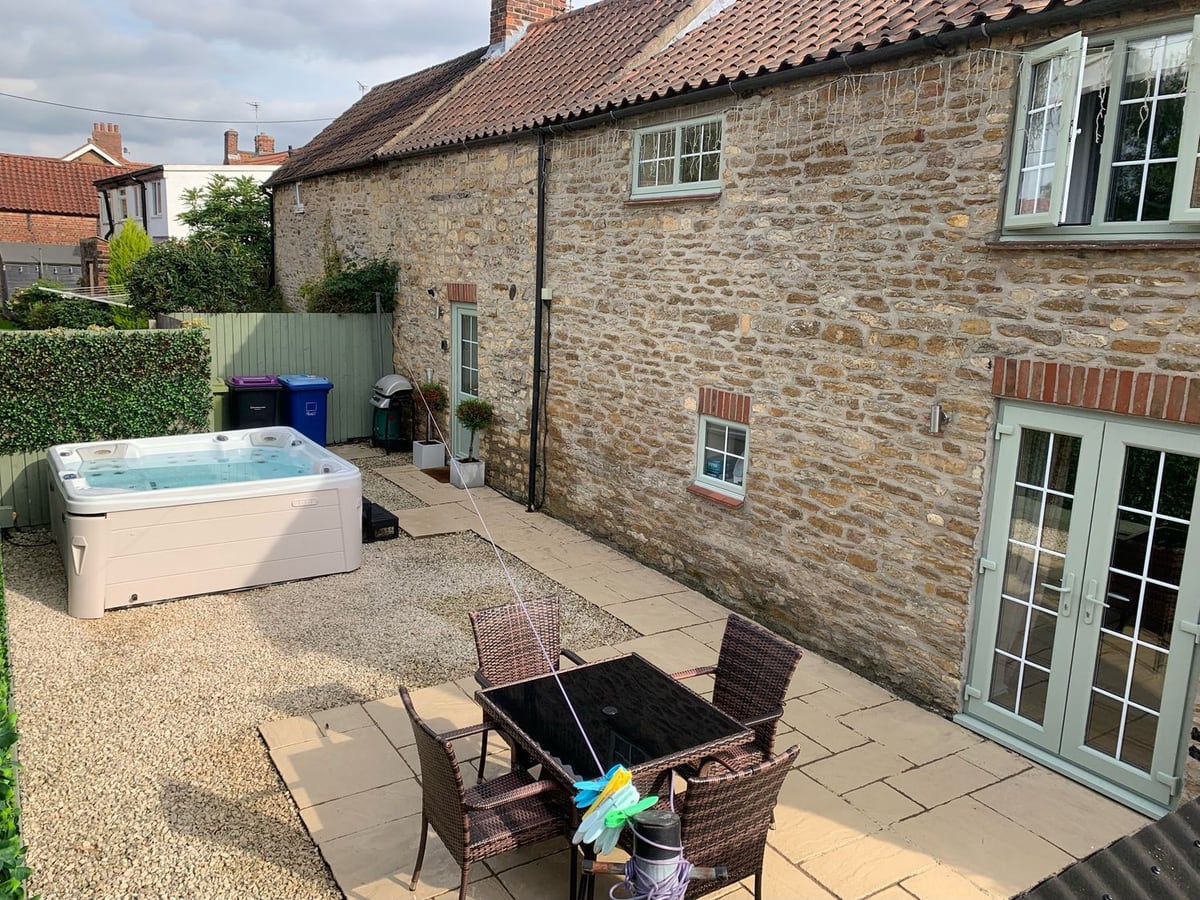 Farriers Cottage's stone rear wall beside a gravel courtyard, dining table and hot tub