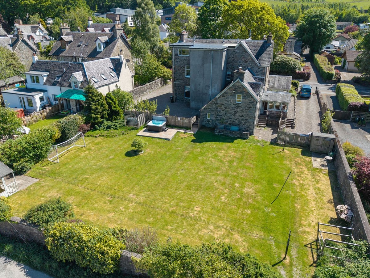 Fernbank House from above, showing its broad rear lawn, fenced hot tub patio and stone exterior