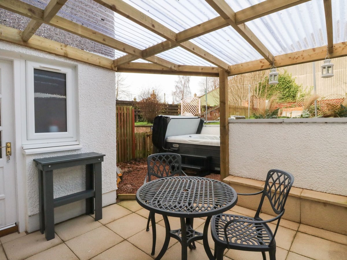 Covered patio seating beside Feus Holiday Cottage, with a hot tub and raised garden beyond